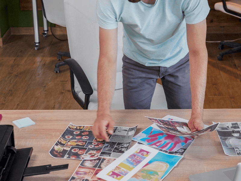 Grafico al lavoro con materiali pubblicitari e campioni di stampa.